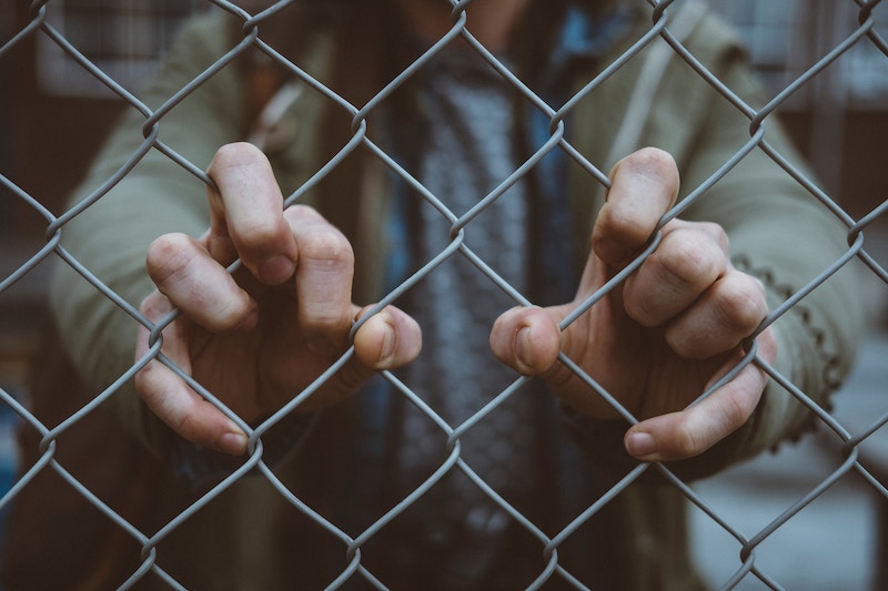 Photo of someone's hands clinging to a chainlink fence. 