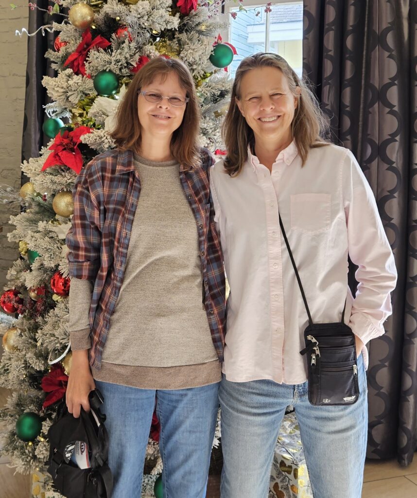 Two women in front of a Christmas tree smiling.